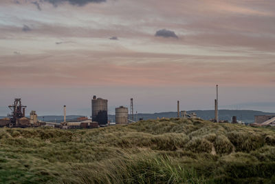 Factory on landscape against sky during sunset