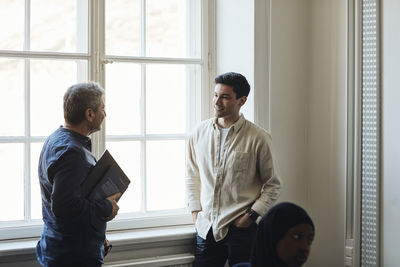 Male teacher talking with student while standing by window in university