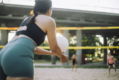 Woman serving volleyball while playing with friend