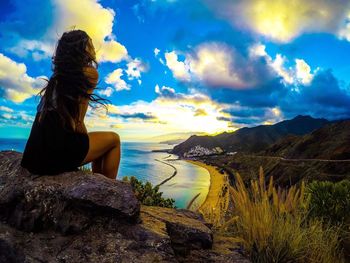 Woman sitting on rock by sea against sky