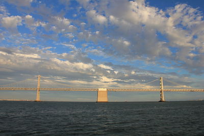 Suspension bridge over sea against cloudy sky