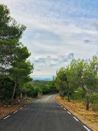 Empty road along trees and plants against sky