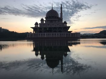 Reflection of shah alam mosque in lake against sky during sunset