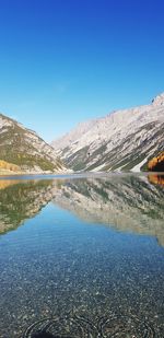 Scenic view of lake and mountains against clear blue sky