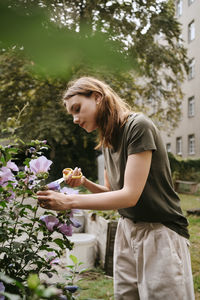 Young woman trimming leaves of flowers with scissor while standing in garden