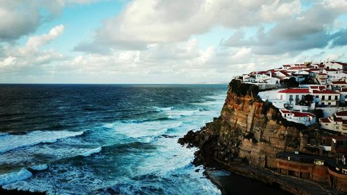 Houses on rock by sea against cloudy sky