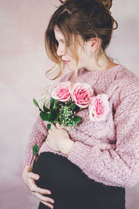 Midsection of woman holding pink rose standing against wall