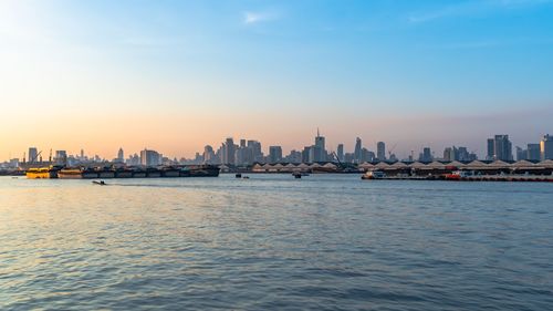 Sea by city buildings against sky during sunset