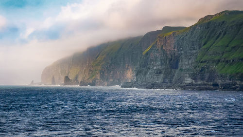 Scenic view of sea with moss covered rocky coastline against sky.