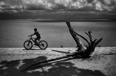 Low section of man riding bicycle on beach against sky