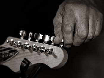 Close-up of man adjusting guitar against black background