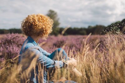 Rear view of woman standing amidst plants on field against sky