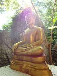 Young woman sitting by statue in forest