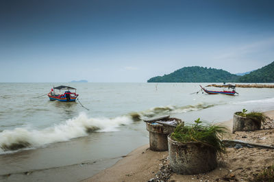 Mid distance view of fishing boats moored in sea against sky