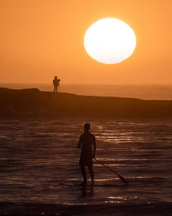 Silhouette man standing on sea against sky during sunset