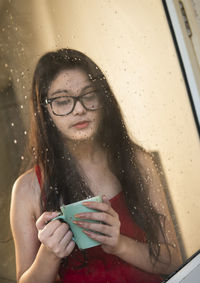 Young woman holding coffee cup seen through mirror