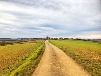 Dirt road amidst field against sky