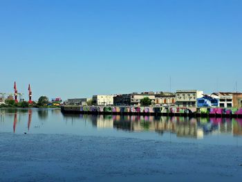 Buildings by lake against clear blue sky