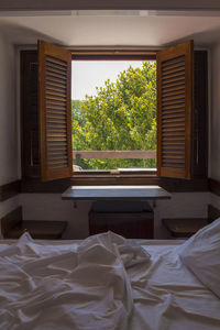 Room with unmade bed and open wooden shutters