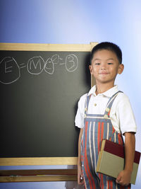 Portrait of smiling boy standing by blackboard against blue background