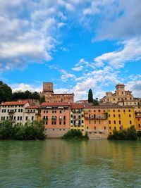 Buildings by river against sky