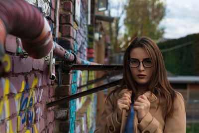 Portrait of young woman wearing eyeglasses while standing by wall