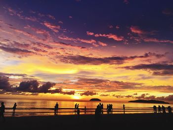 Silhouette people on beach against dramatic sky