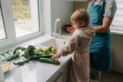 Mother and little child toddler are washing vegetables together in the kitchen for cooking dinner.