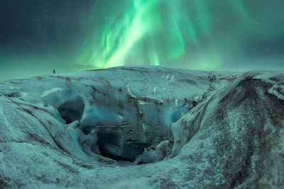 Uneven ice formation of vatnajokull glacier with tourist located against night sky with bright green aurora borealis on winter day in iceland