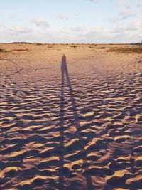 Shadow of person on sand at beach against sky