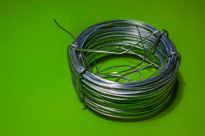 High angle view of rolled up metallic wire on green background