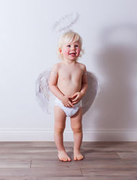 Portrait of shirtless boy standing against wall at home