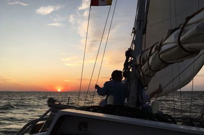 Woman sailing on sea against sky during sunset