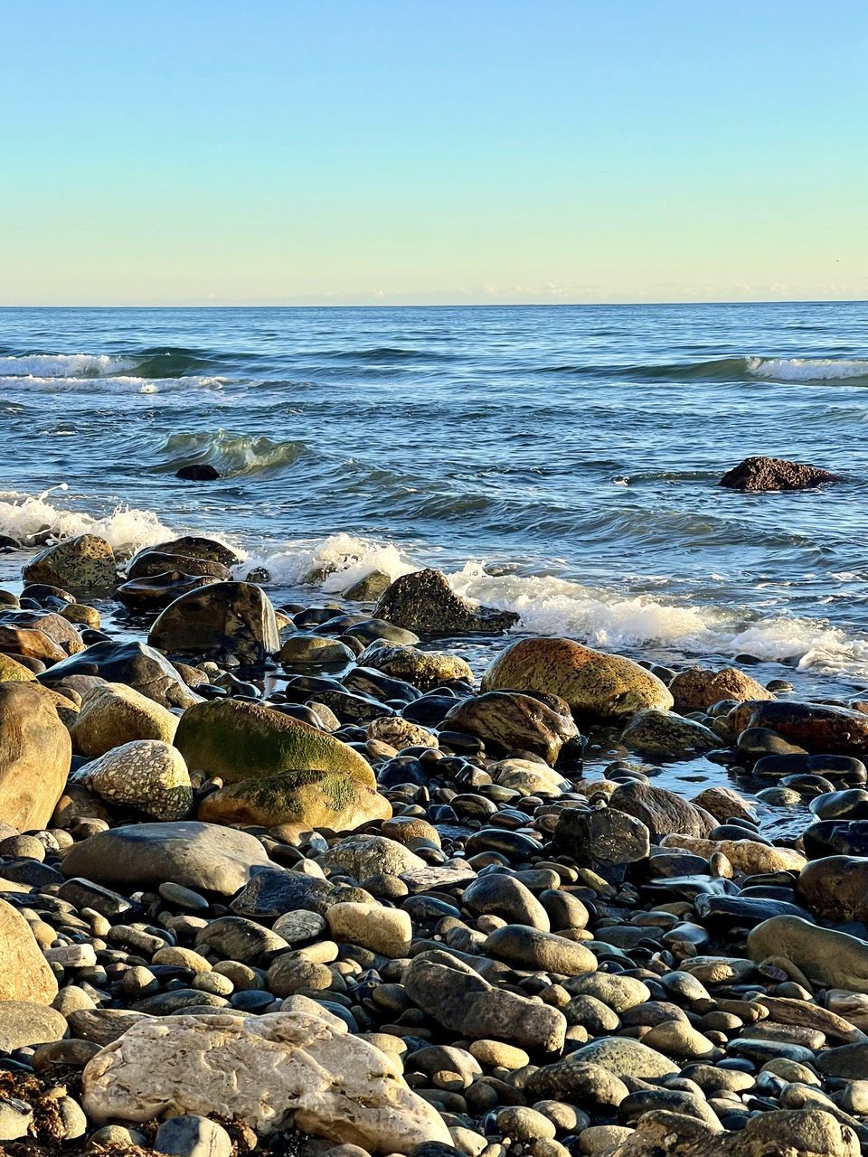 sea, water, rock, beach, land, body of water, shore, sky, nature, beauty in nature, horizon over water, scenics - nature, horizon, ocean, coast, tranquility, wave, tranquil scene, stone, clear sky, sand, no people, pebble, motion, idyllic, day, outdoors, sunlight, wind wave, seascape, coastline, non-urban scene, travel destinations