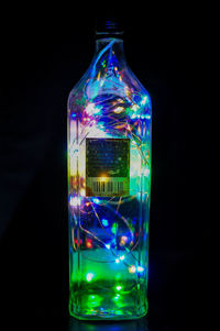 Close-up of illuminated glass bottle against black background