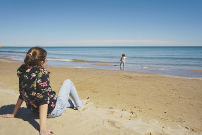 Rear view of woman standing at beach against clear sky