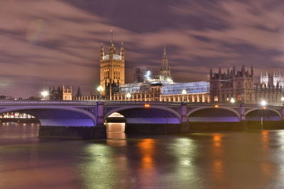 Illuminated bridge over river against sky in city at night