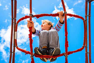 Low angle view of boy balancing on rope against sky in playground
