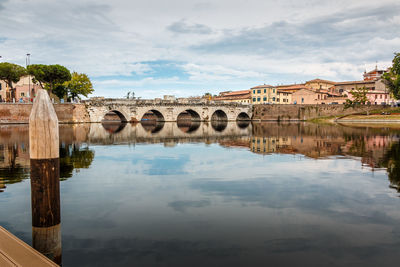 Arch bridge over river in city against sky