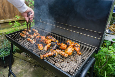 Cropped hand preparing meat on barbecue grill