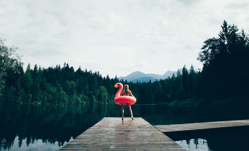 Rear view of woman on pier over lake against sky