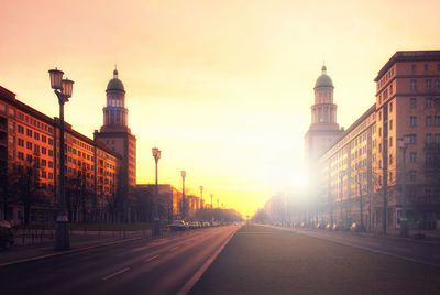 Road amidst buildings against sky during sunset