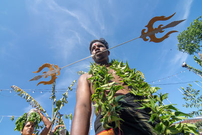 Low angle view of man holding plants against sky