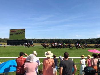 People watching horse racing against sky