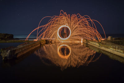 Illuminated wire wool by lake against sky at night