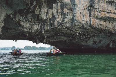 People on boats below rock formations in sea