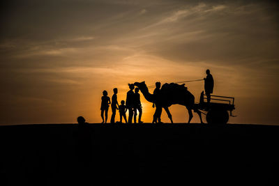 Silhouette people riding horses against sky during sunset