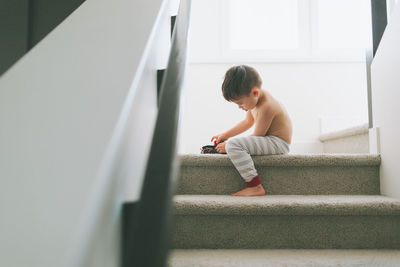 Shirtless boy sitting on staircase at home