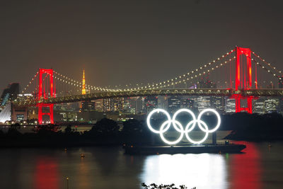 Illuminated bridge over river in city at night