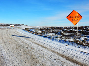 Road sign on snow covered landscape against blue sky